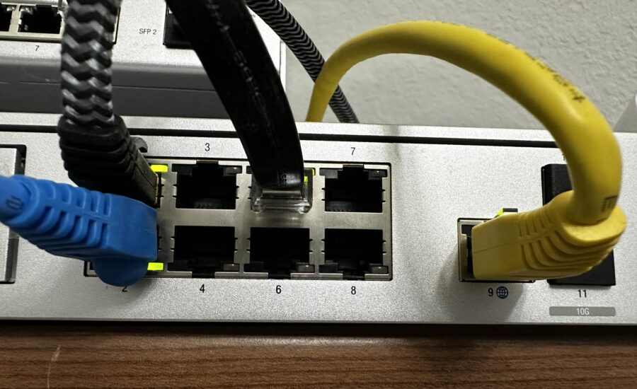 Network switch with blue and yellow Ethernet cables plugged into ports, showing port numbers and cables in use.